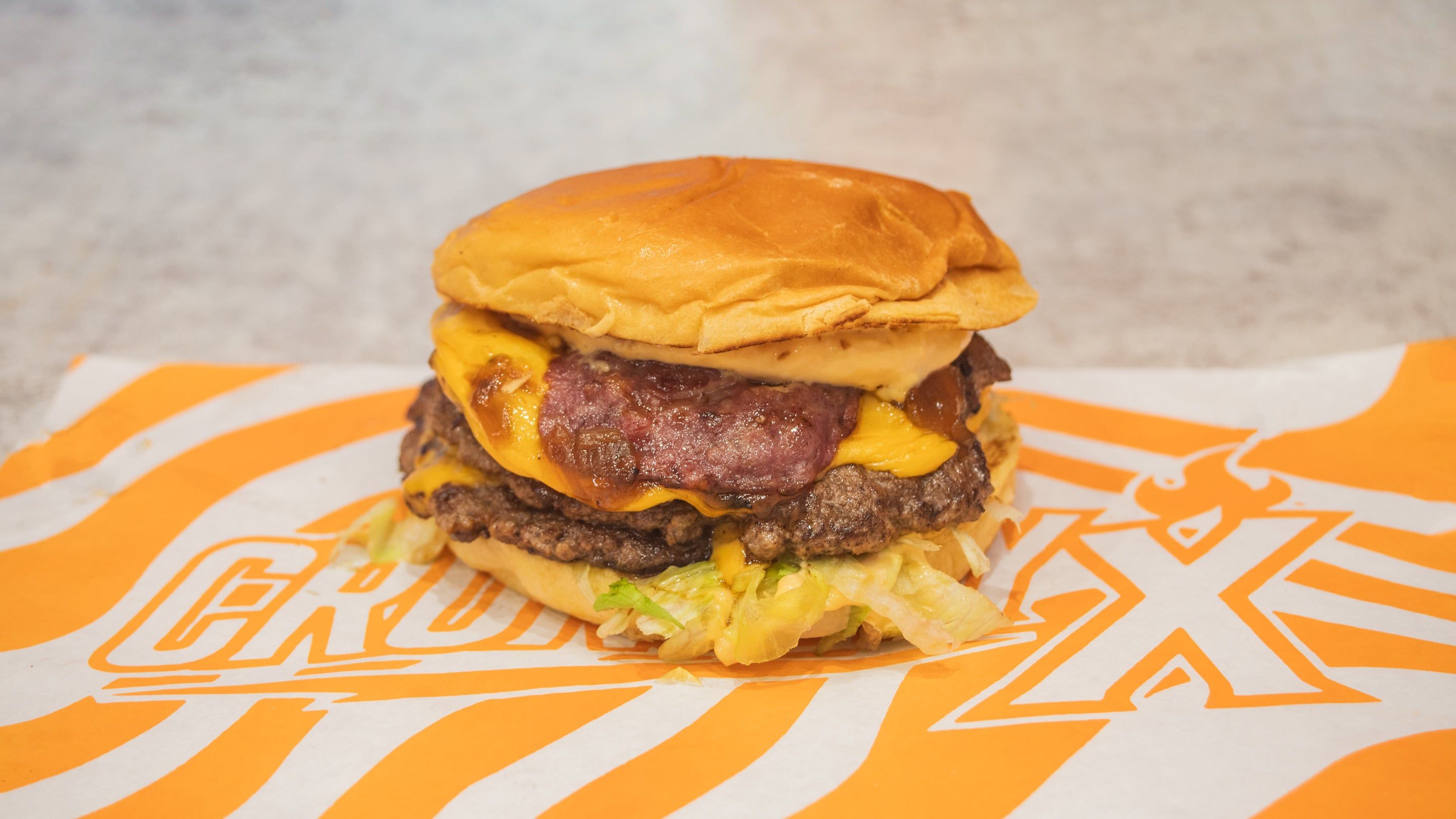 Le Gourmand : smash burger triple steak et bacon posé sur le papier Crunchy X